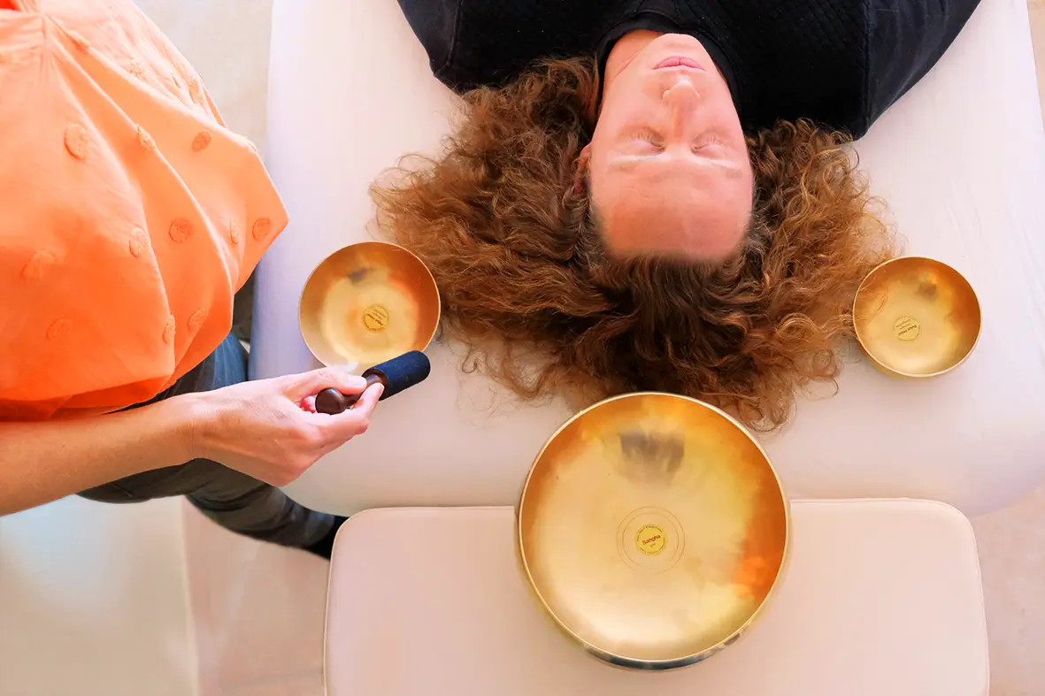 Séance de massage sonore sur un client chez Claire Résonance. Séance vue de haut, le client est entouré de trois bols que Claire fait sonner.